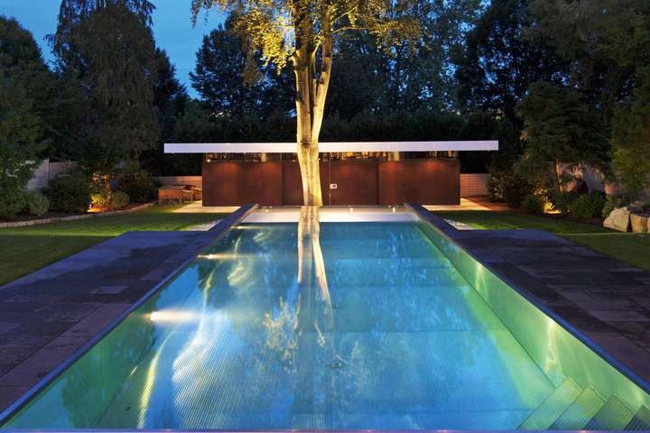 Hausseitig schließt der streng geometrisch geformte Edelstahl-Pool bündig mit der Terrasse ab. Die gartenseitige Beckenkante gestalteten die Designer der Firma SSF.Pools als Infinity-Überlaufbecken.
